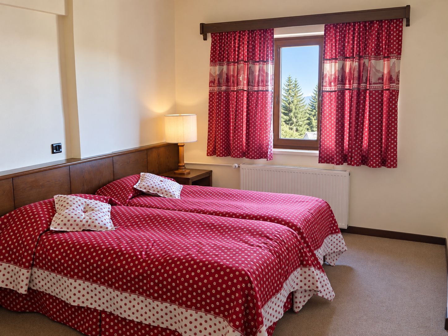 Una habitación con dos camas, una mesita de noche, una lámpara y una ventana con cortinas.
