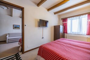 Un dormitori amb un llit, televisió penjada a la paret, armari i finestra amb cortines.