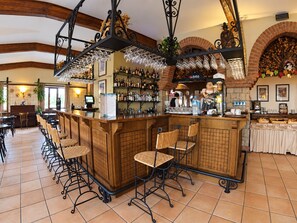 Una zona de bar con una barra alargada, varios taburetes y una variedad de botellas y vasos.