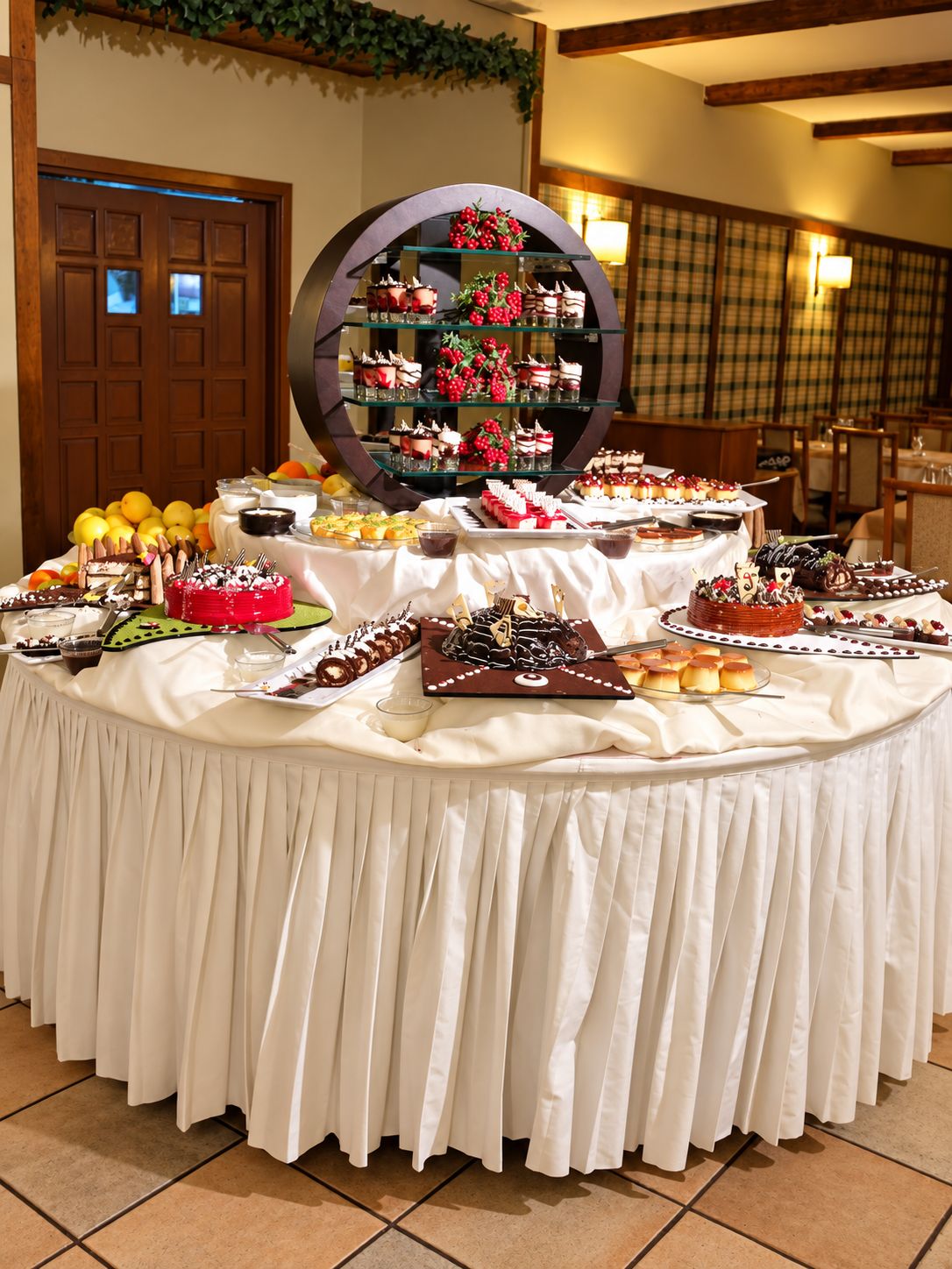 A buffet table with various desserts and fruits, a large decorative mirror, and a wooden door in the background.