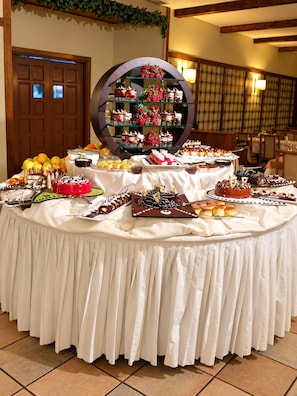Una mesa de buffet con diversos postres y frutas, un espejo decorativo grande y una puerta de madera al fondo.