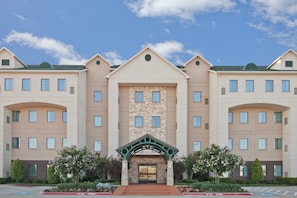 A multi-story hotel with a central entrance, symmetrical windows, and a landscaped front garden. - King Studio Suite w/ Hot Breakfast, Pool & Hot Tub (Plano)