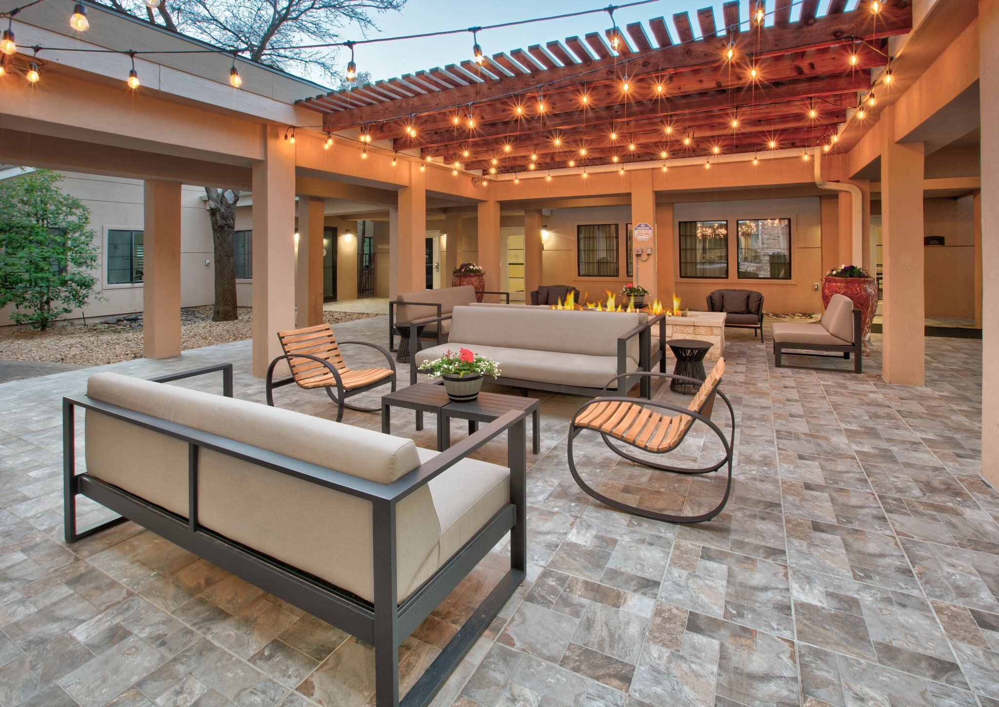 Un espace extérieur aménagé en terrasse, doté d’une pergola, de guirlandes lumineuses et de différents types de sièges, notamment des canapés et des fauteuils.