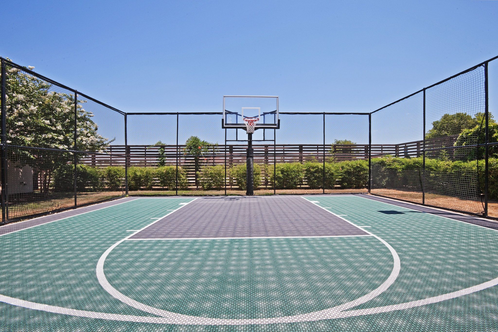 An outdoor basketball court with a net, surrounded by a fence and trees.