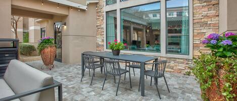 Une terrasse avec une table et des chaises, des plantes en pot et un sol recouvert de carreaux de pierre.