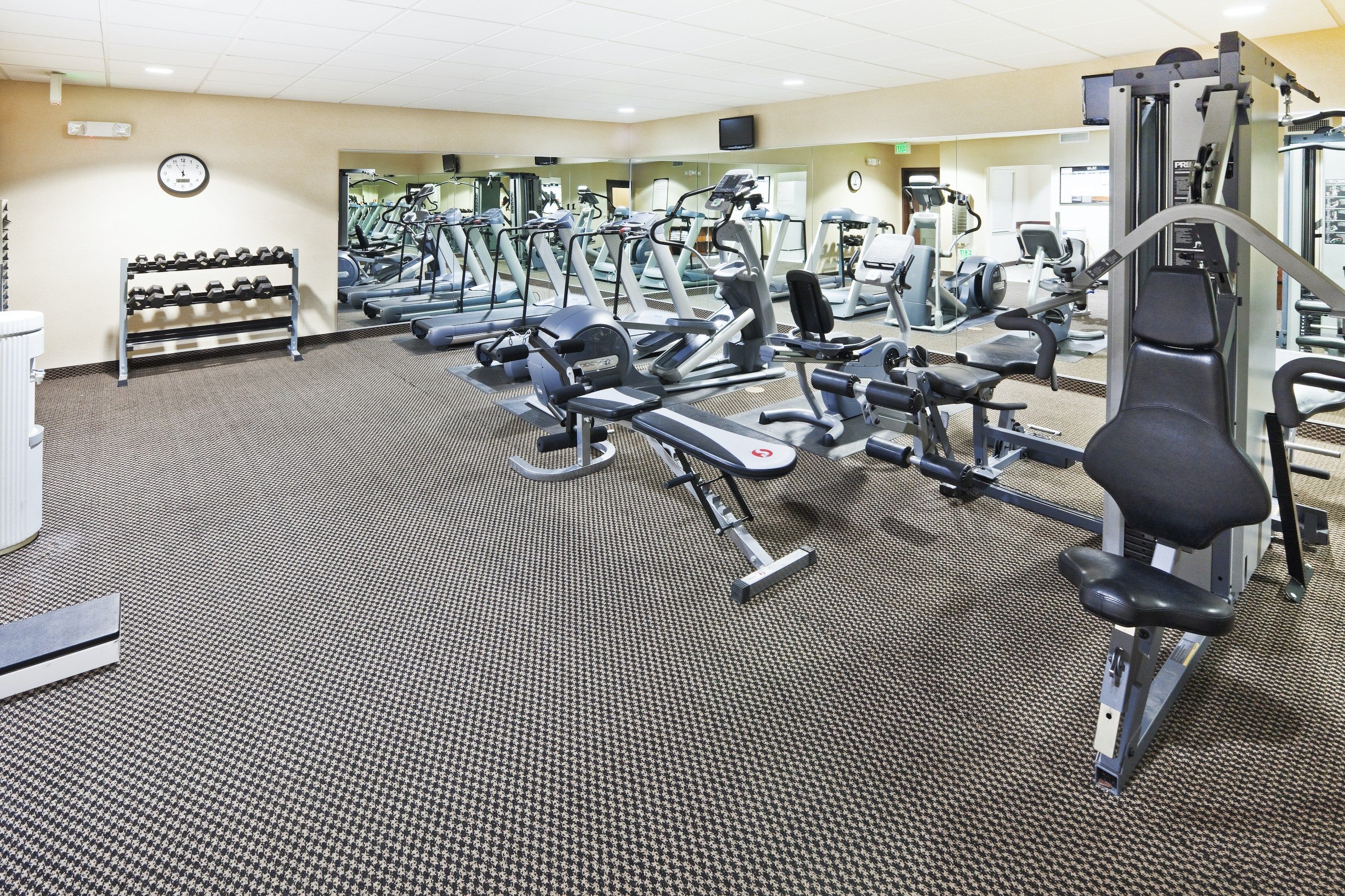A gym with various exercise machines, a clock on the wall, and a shoe rack.