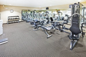 Une salle de sport équipée de divers appareils d’exercice, une horloge au mur et un porte-chaussures.