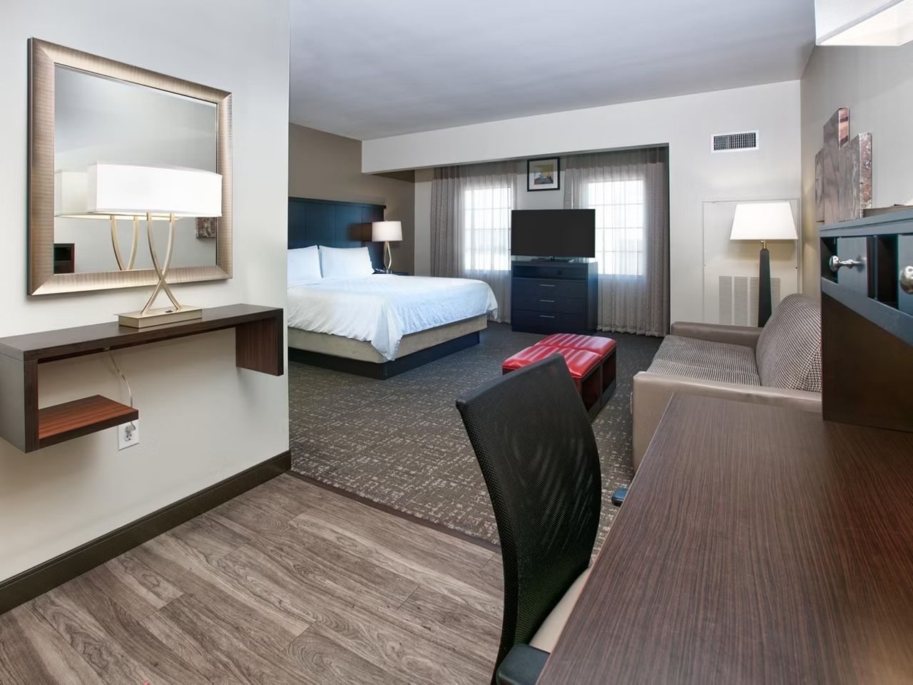 Ein Hotelzimmer mit Bett, Schreibtisch, Sessel, Fernseher und Spiegel.