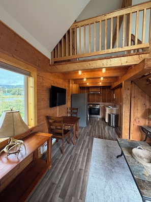 Interno di una baita in legno con zona pranzo, cucina e un balcone.