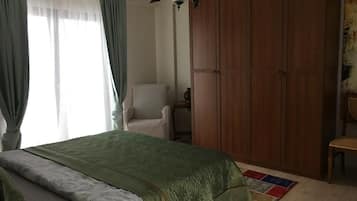 A bedroom with a bed, a chair, a wardrobe, and a window with curtains.