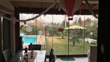 A covered patio with a view of a swimming pool and garden.