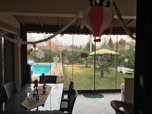 A covered patio with a view of a swimming pool and garden.