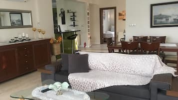 A living room with a sofa, a glass coffee table, a dining area with chairs, and a kitchen in the background.