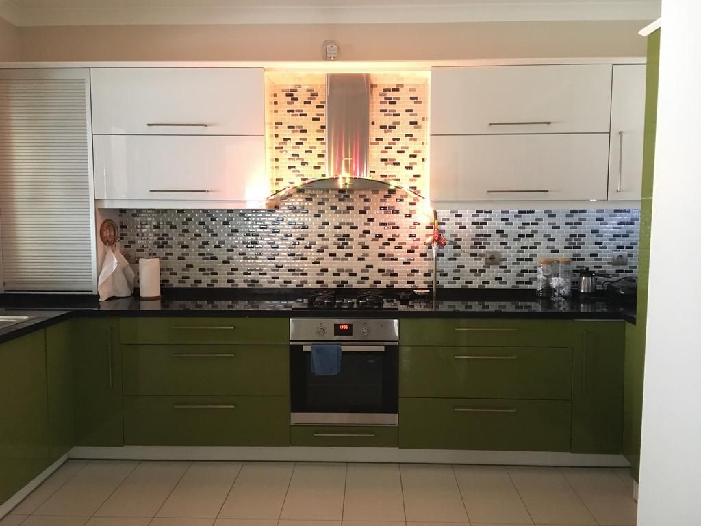 A kitchen with green cabinets, a tiled backsplash, and a stainless steel oven.