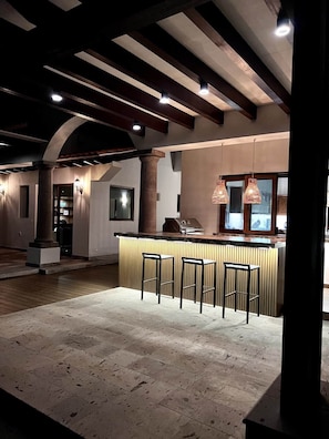Un espace bar avec un comptoir et des tabourets, un plafond en bois avec des poutres apparentes et un sol en pierre.