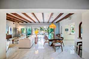 An open-plan living area with a dining table, sofas, and a large window offering a view of greenery. - Magnificent Canal House w/ Dock & Adjacent Golf (Nuevo Vallarta)