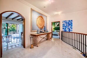 A hotel lobby with a marble floor, a wooden console table, a large mirror, and a staircase with a black railing. - Magnificent Canal House w/ Dock & Adjacent Golf (Nuevo Vallarta)