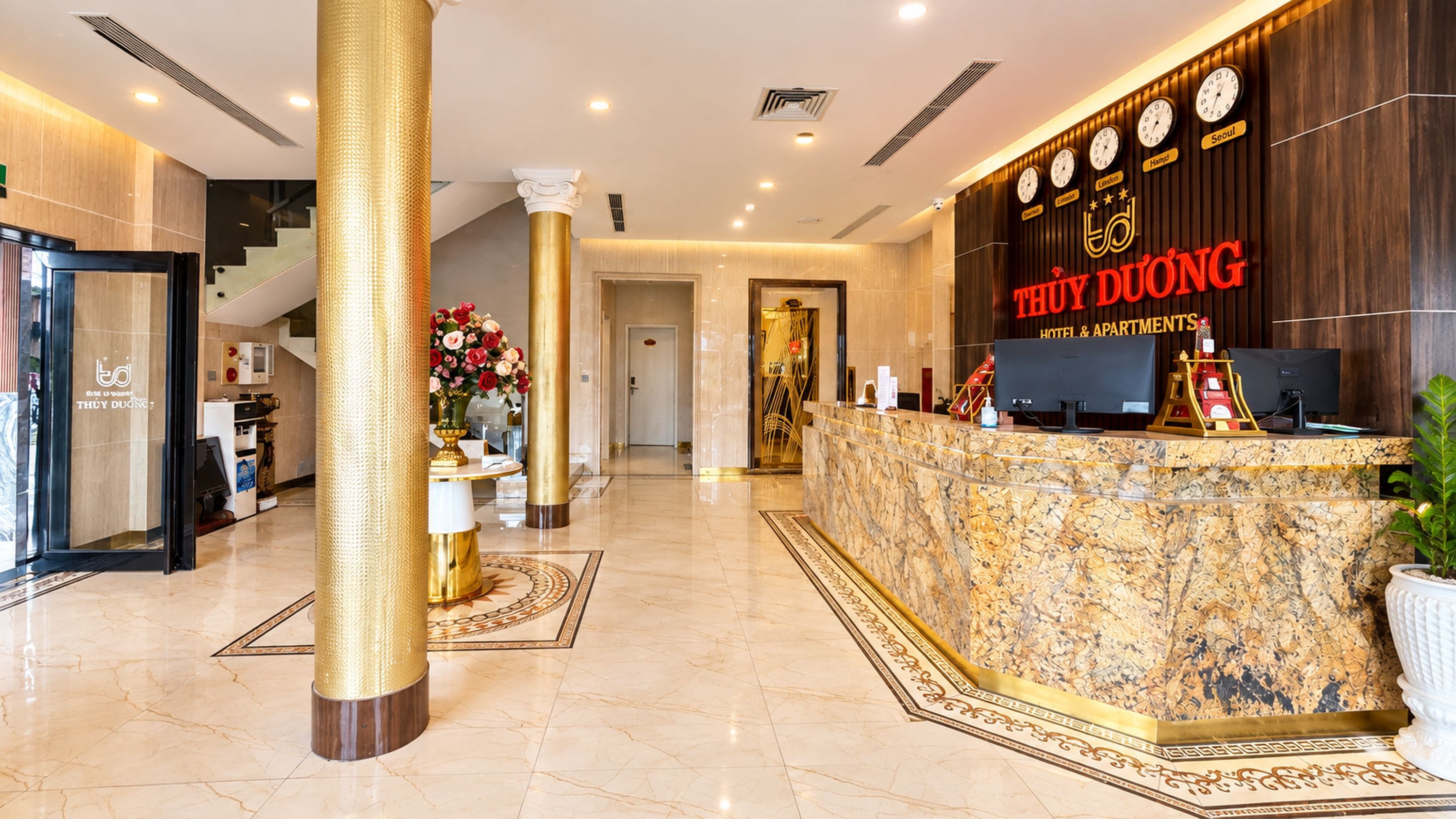 Ein Hotel-Empfangsbereich mit einem Marmor-Empfangstresen, einer Uhrausstellung und einer Treppe zu den oberen Etagen.