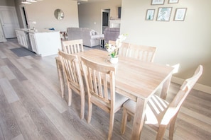 Un comedor con mesa y sillas de madera, una cocina al fondo y una sala de estar con sofá y mesa de centro.