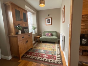 Una habitación acogedora con un armario de madera, un sofá verde, un tapete estampado y una chimenea.