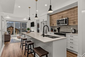 A modern kitchen with a large island, wooden cabinets, and stainless steel appliances. - Mountains Plenty | Luxury Hot Tub and Sauna (Canmore)