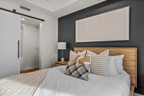A bedroom with a bed, a nightstand, a lamp, a wardrobe, and a large framed picture on the wall. - Mountains Plenty | Luxury Hot Tub and Sauna (Canmore)
