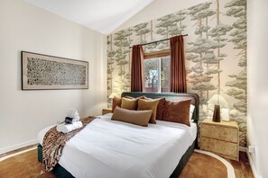 Une chambre d’hôtel avec un grand lit, une œuvre d’art accrochée au mur, une fenêtre avec des rideaux, une lampe de chevet et une petite table de chevet.