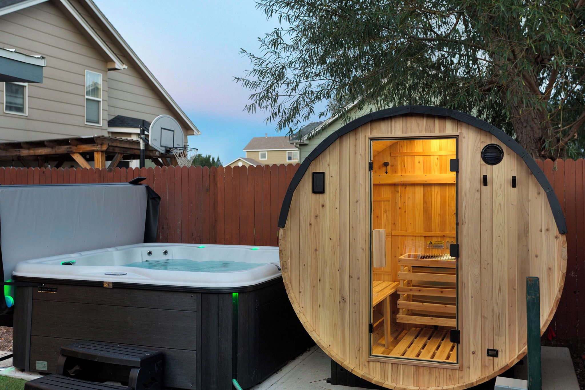 A wooden sauna structure with a bench inside, a hot tub outside, and a wooden fence in the background.
