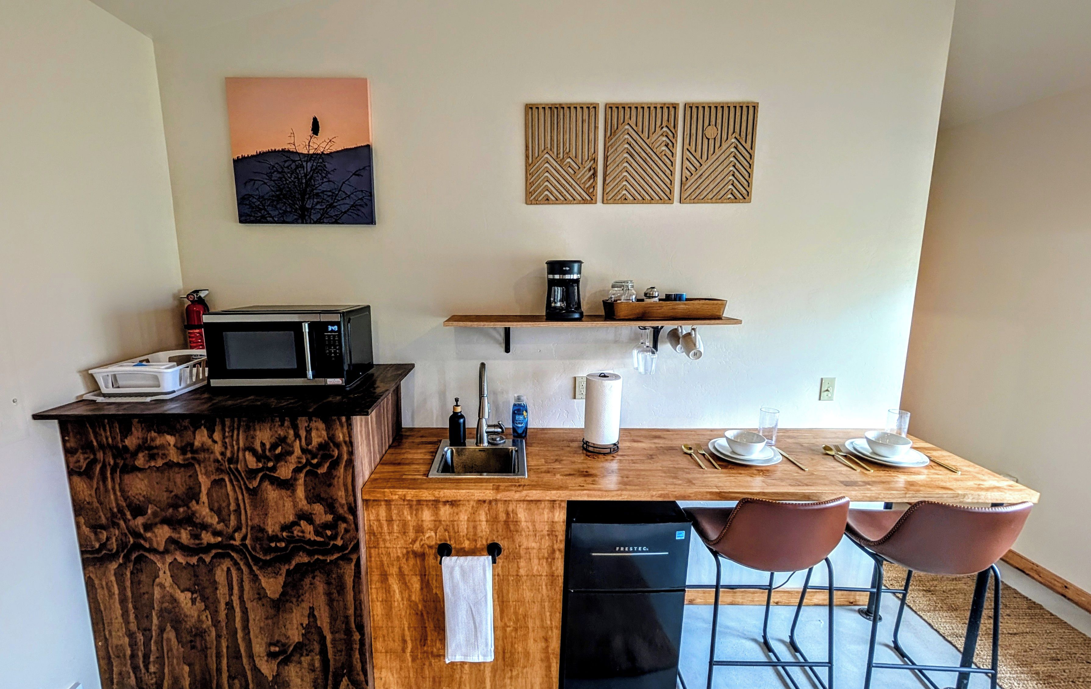 A compact kitchen with a microwave, coffee maker, and bar stools.