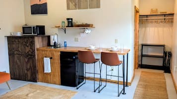 A compact kitchen with a microwave, coffee maker, and a sink. There are two bar stools and a small table with a few dishes.