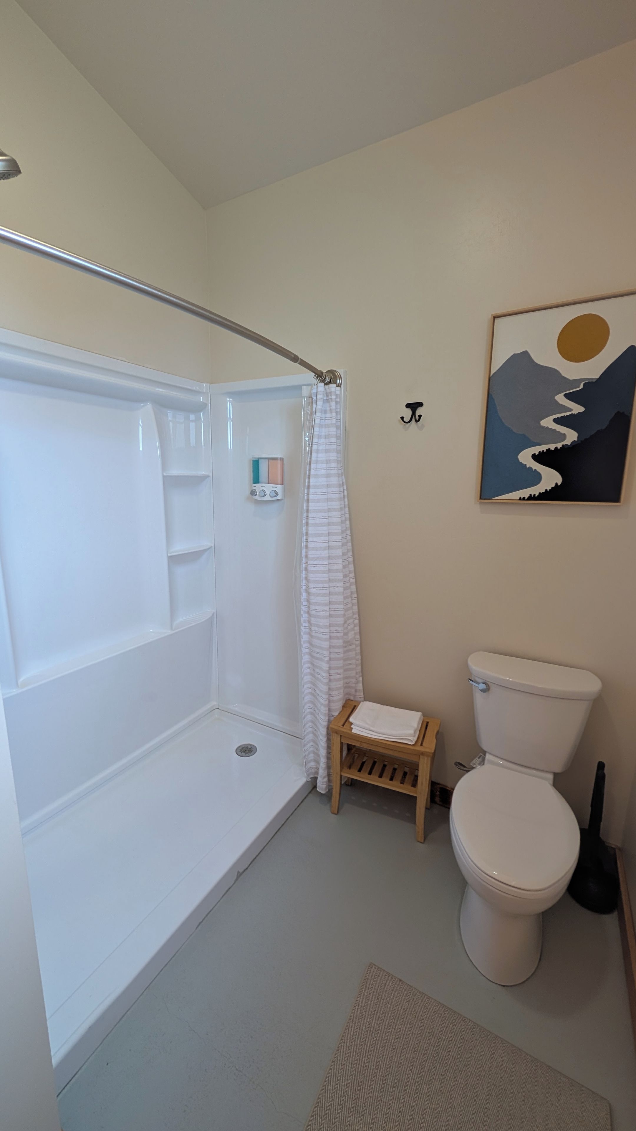 A bathroom with a shower, toilet, and a small wooden stool.
