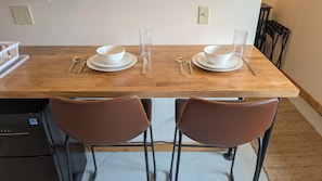 Een eettafel met twee witte kommen, een glas en bestek. Er staan twee bruine stoelen met metalen poten.