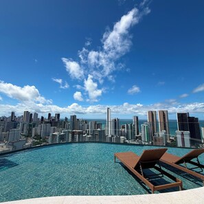 Una piscina infinitum a la terrassa amb gandules, amb vista a un skyline urbà ple d'edificis alts.