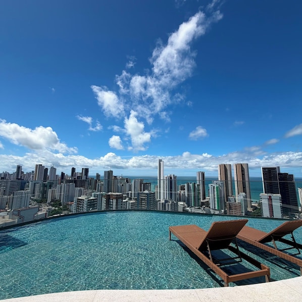 A rooftop infinity pool with lounge chairs, overlooking a city skyline with high-rise buildings. - Edf Praia de Gameleira (Recife)
