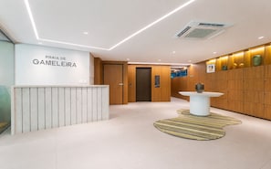 A reception area with a reception desk, a wall-mounted sign, a wooden panel wall, a patterned rug, and a wall-mounted air conditioning unit. - Edf Praia de Gameleira (Recife)
