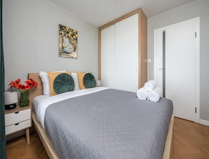 A neatly made bed with a grey quilt, a bedside table with a vase of flowers, and a painting on the wall. - Spacious Apartment in Central Warsaw (Warsaw)