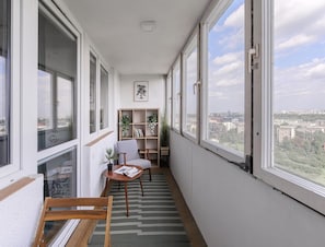 A narrow balcony with a view of a cityscape, a wooden chair, a small table with a magazine, and a bookshelf with plants. - Spacious Apartment in Central Warsaw (Warsaw)