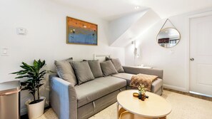 A modern living room with a grey sofa, a small round table, a potted plant, and a painting on the wall. - Casa Marlow by Avantstay Urban San Diego Retreat Near Balboa Park + Beaches + Downtown (San Diego)