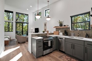 A modern kitchen with a central island, built-in appliances, and large windows offering views of trees. - Birchwood | Hocking Hills, Luxury, Hot Tub, Pets (McArthur)