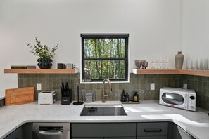 Eine moderne Küche mit eingebautem Spülbecken, einem Toaster, einer Mikrowelle und einem Fenster mit Blick auf Bäume.