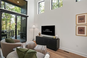 A modern living room with a flat-screen TV, comfortable seating, and a view of the outdoors. - Birchwood | Hocking Hills, Luxury, Hot Tub, Pets (McArthur)