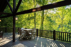 A wooden deck with a table and chairs, surrounded by a railing, overlooking a dense forest. - Luna Moth | Hocking Hills, Firepit, Pool Table (Logan)