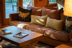 A leather sofa with a butterfly pillow, a wooden coffee table, and a patterned rug. - Luna Moth | Hocking Hills, Firepit, Pool Table (Logan)