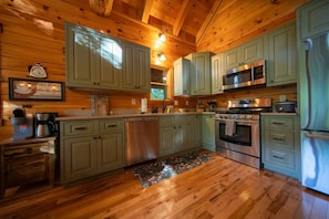 A wooden-paneled kitchen with green cabinets, stainless steel appliances, and a wooden floor. - Luna Moth | Hocking Hills, Firepit, Pool Table (Logan)