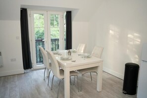 A dining area with a white table set for four, a sliding glass door leading to a balcony, and a black trash bin. - Jacobs court 47 (Crawley)