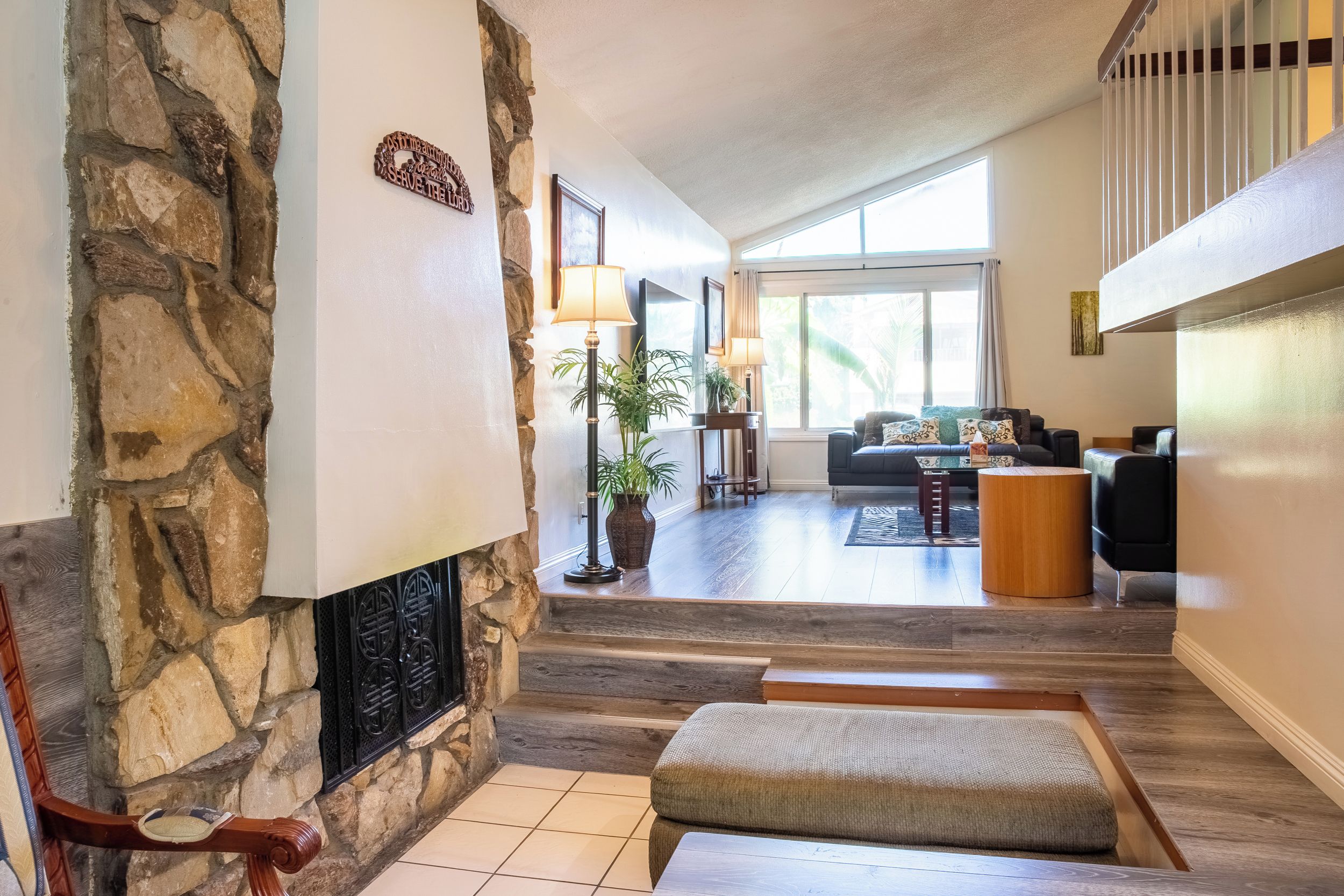 A spacious living area with a stone fireplace, a sofa set, and a large window providing natural light.
