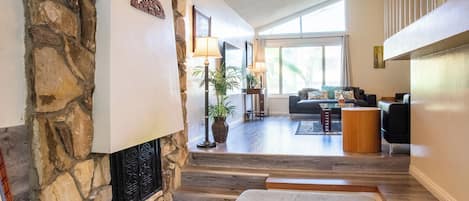 A spacious living area with a stone fireplace, a sofa set, and a large window providing natural light.