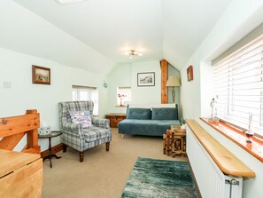 A cozy room with a plaid armchair, a blue sofa, a wooden table, and a window with blinds. - Beck Cottage (Sheringham)