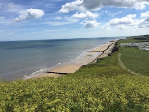 A coastal landscape with a beach, a sea wall, and a field of yellow flowers. - Beck Cottage (Sheringham)