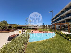 A modern outdoor pool area with a clear blue sky, surrounded by well-maintained grass and plants. - Beach Class Solare Muro Alto (Ipojuca)